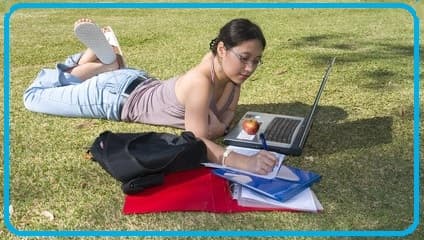 girl on the grass studying (English?) on her computer