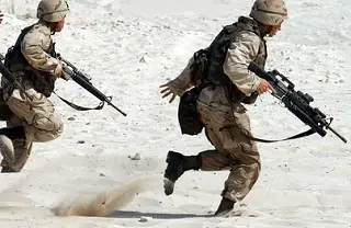 Camouflaged soldiers with automatic weapons running through the desert