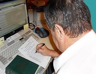 class preparation: man taking notes while using a book and computer.