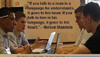 4 men in a serious conversation. Quote on wall: "If you talk to a man in a language he understands, it goes to his head. If you talk to him in his language, it goes to his heart."-- Nelson Mandela