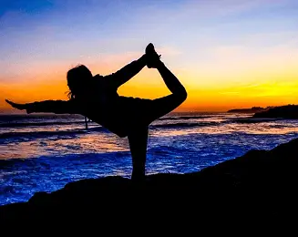 a difficult yoga pose by the ocean at sunset